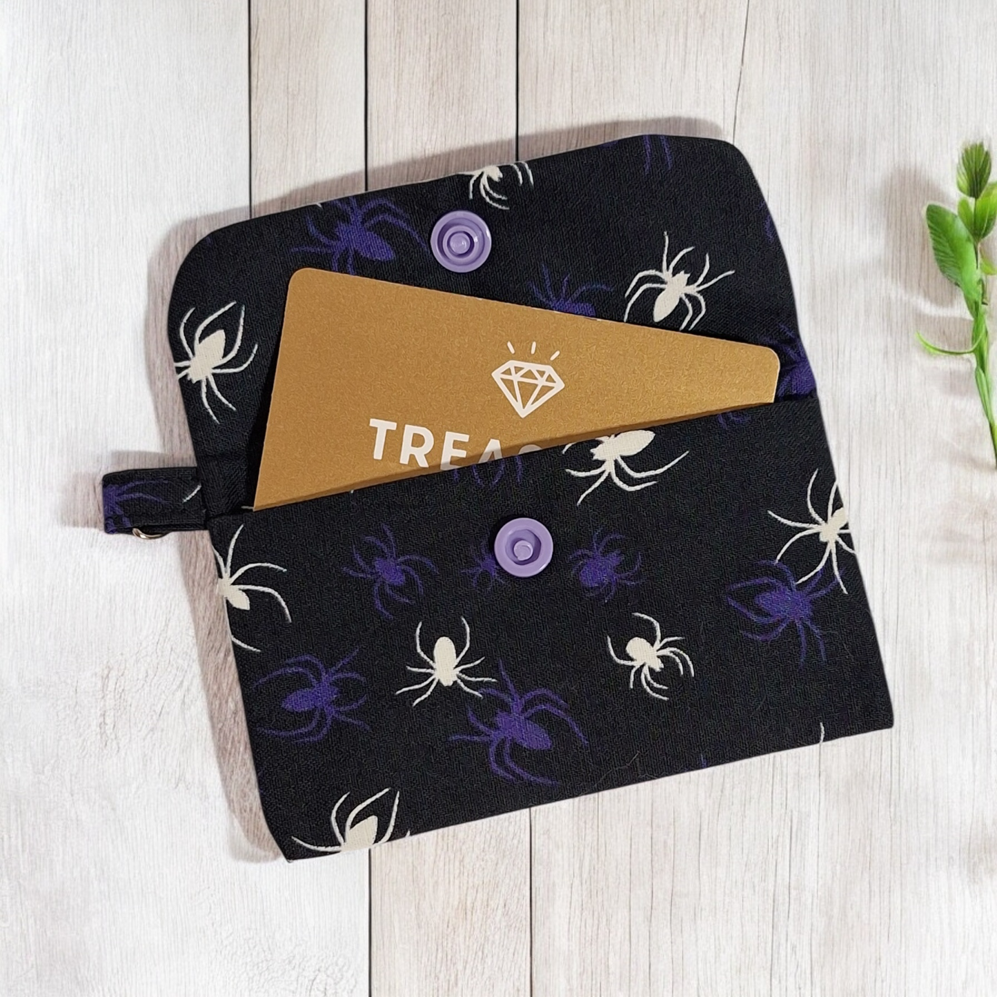 Black pouch with spider pattern containing a card for display purposes on a white wooden surface.