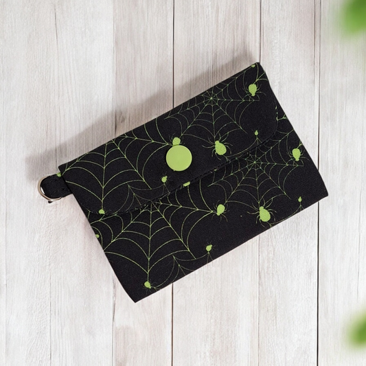Black pouch with green spider web pattern on a light wooden surface