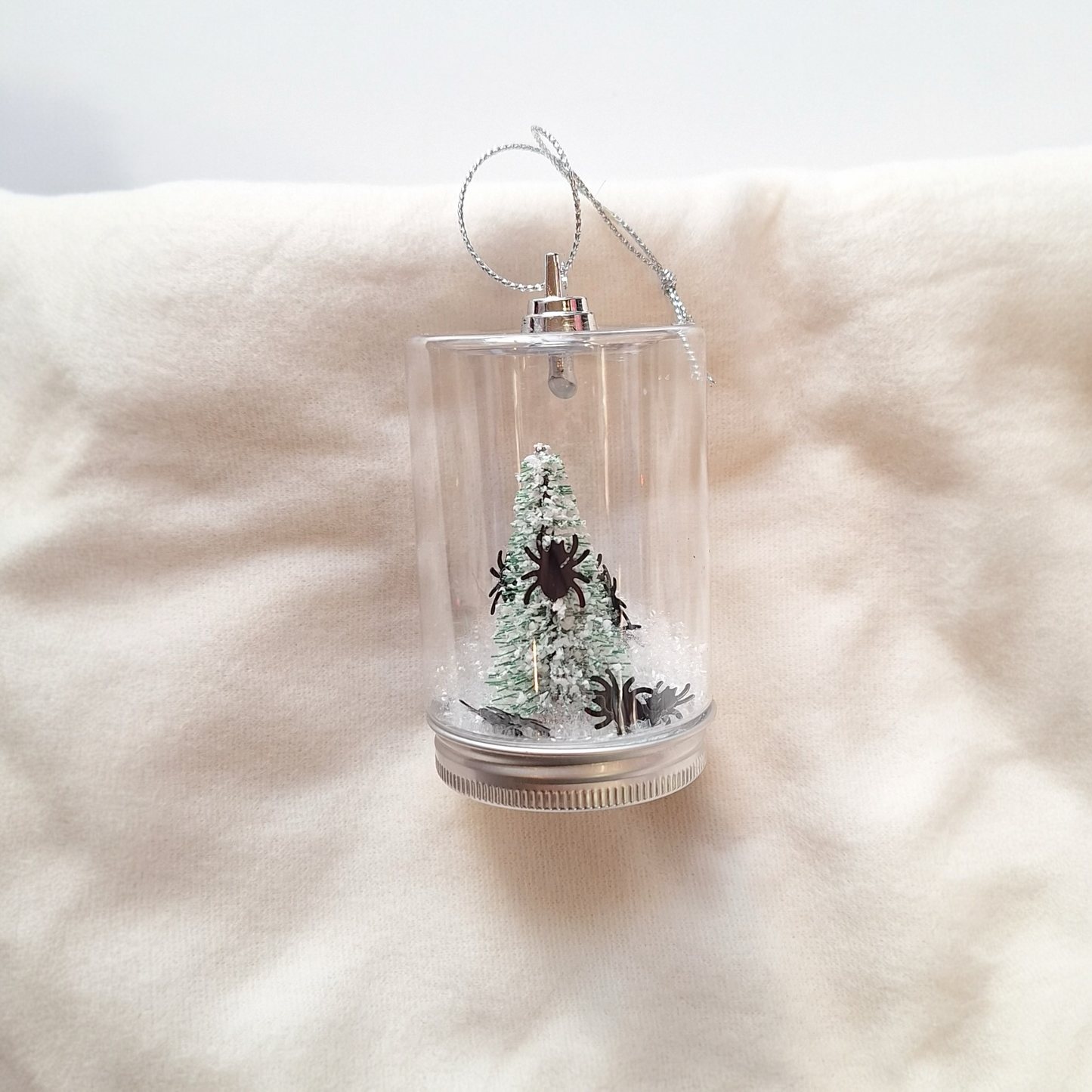 Clear plastic ornament with a miniature Christmas tree and spider on a soft white background