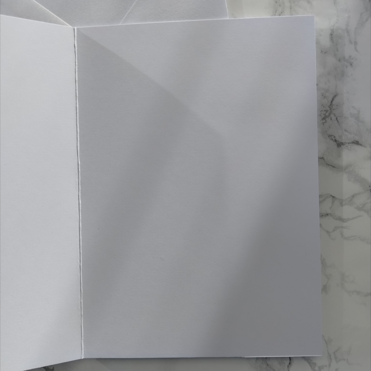 A blank white folded paper card or envelope laid flat on a white and gray marble surface.