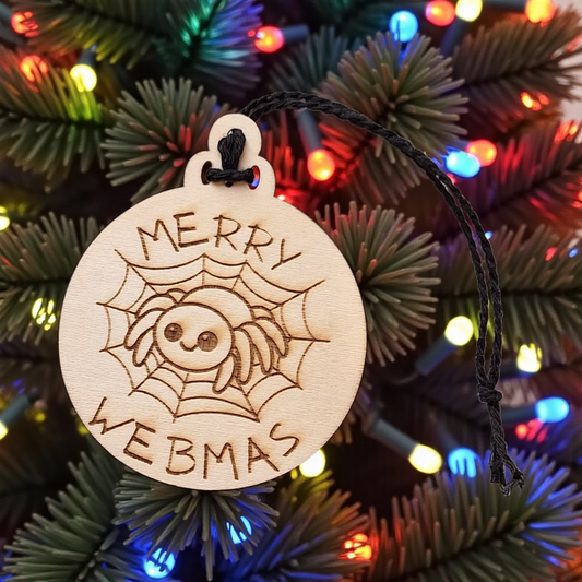 Wooden ornament with spider design and 'Merry Webmas' text on a Christmas tree background.