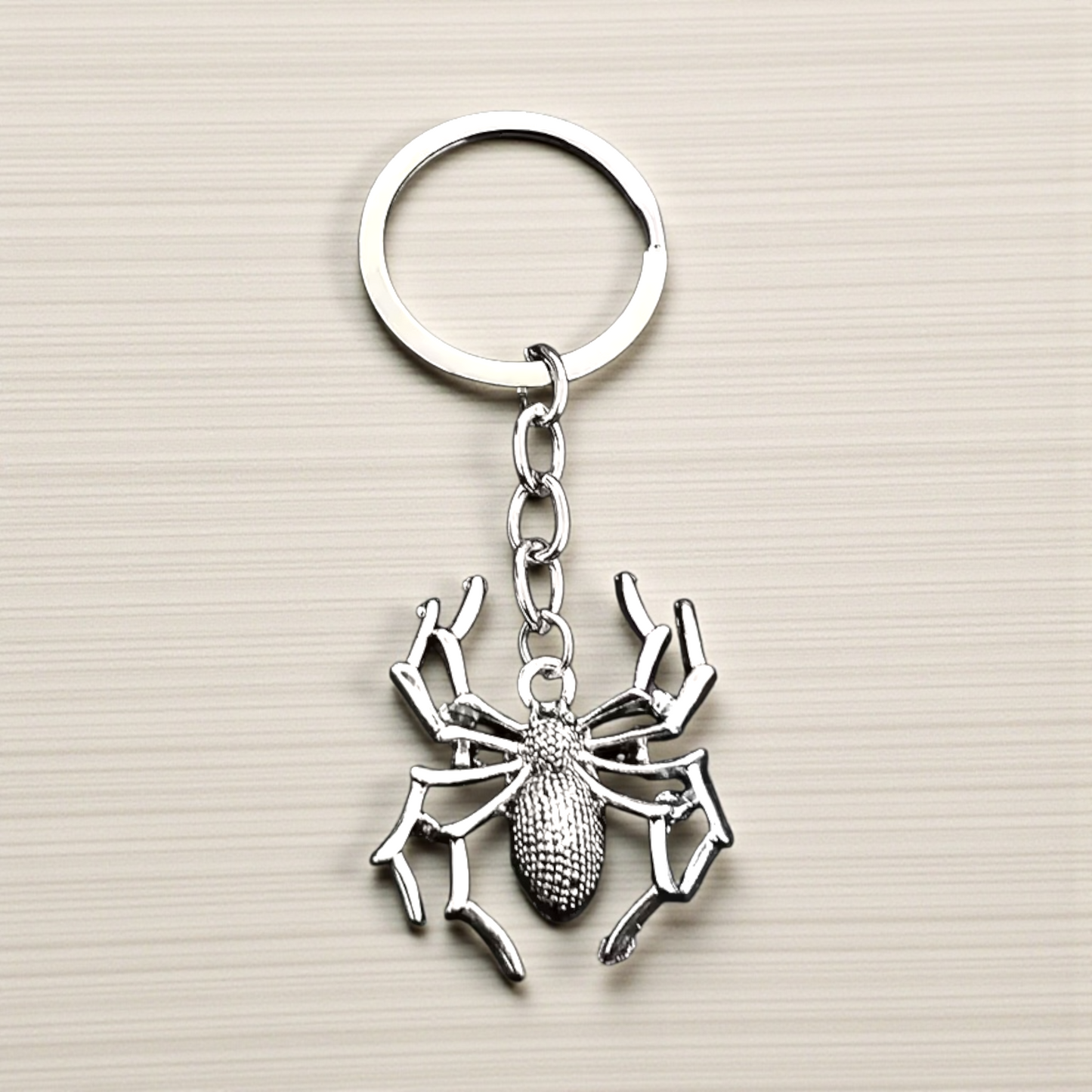 Silver spider keychain on a beige background