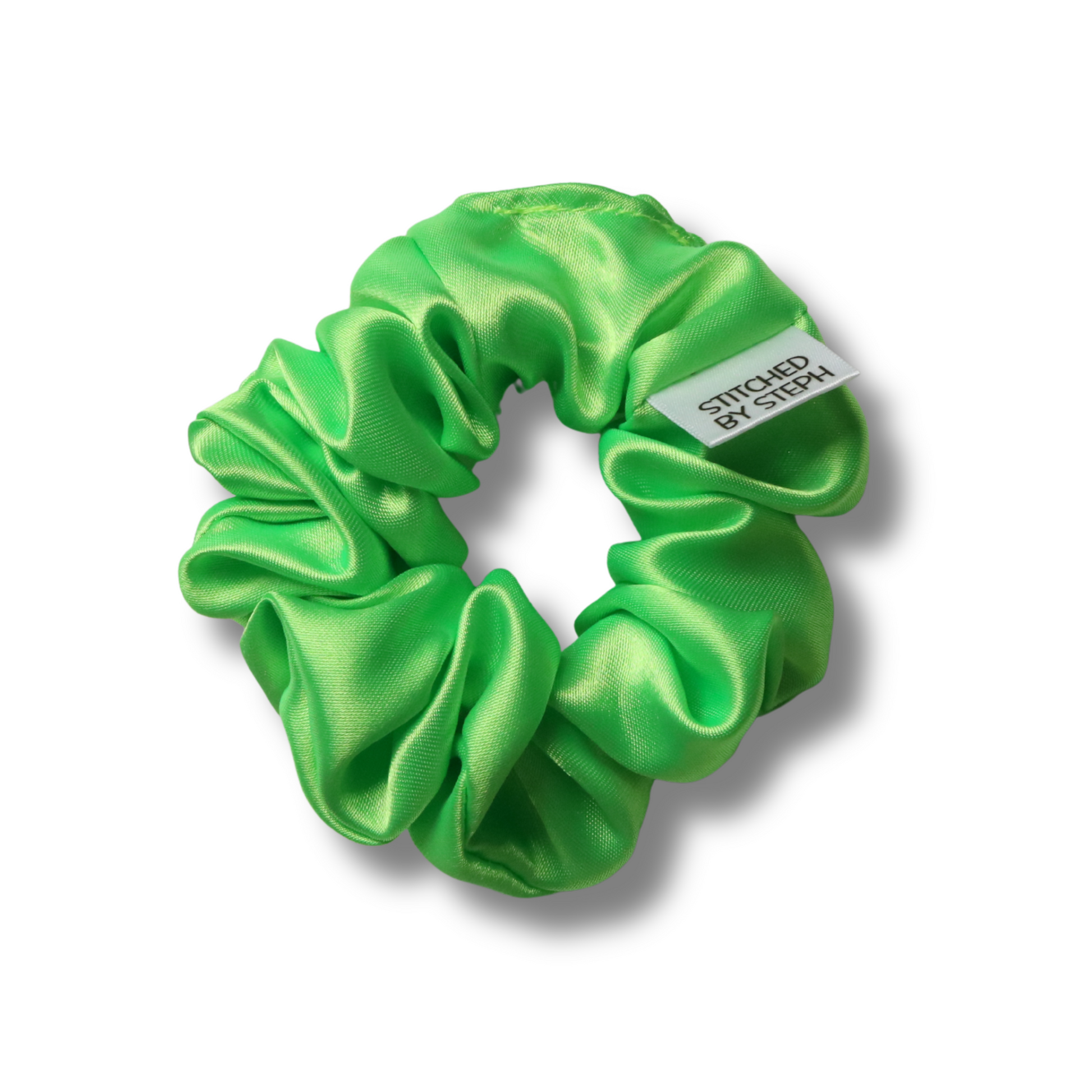 A bright green satin hair scrunchie with a small white tag that reads 'STITCHED BY STEPH', shown on a clean white background with a soft drop shadow.