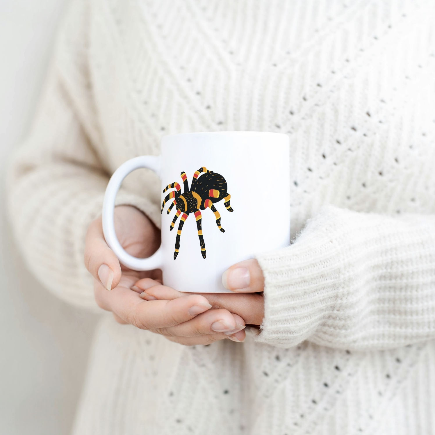 Person holding a mug with a spider design against a plain background